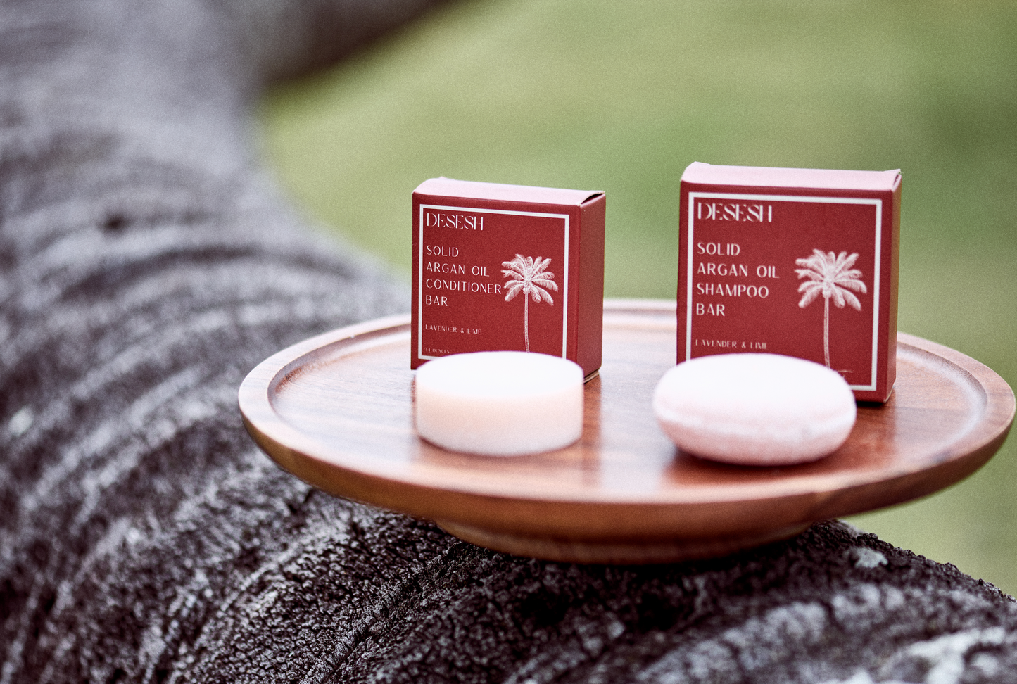 This image shows salon quality Argan Oil Shampoo bars with plastic free biodegradable packaging for a more sustainable eco friendly zero waste hair care routine. In the image there is a Lavender and Lime solid shampoo bar and a solid conditioner bar on a wood surface.