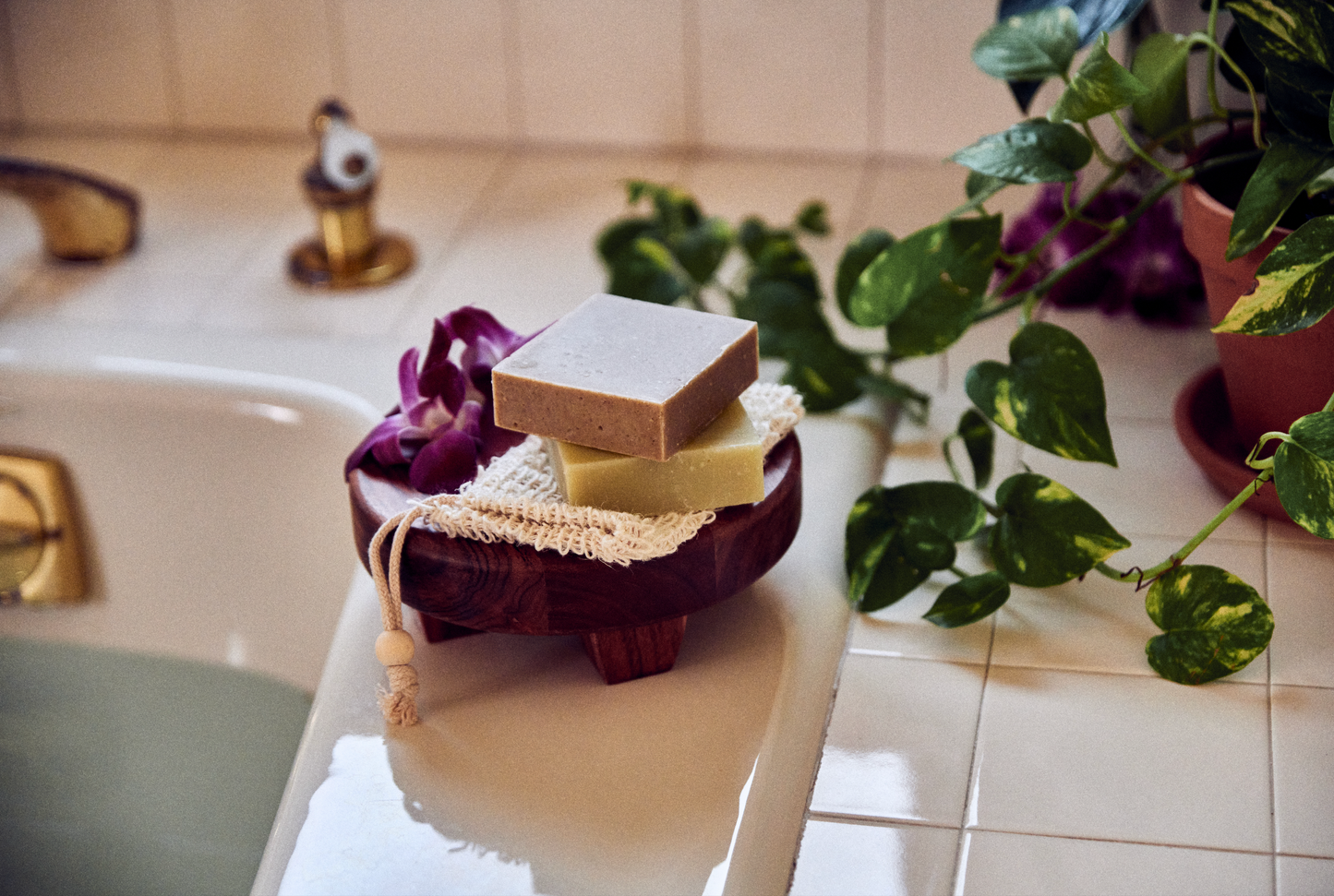 This image shows a cotton sisal soap saver bag. It is used for soap bars and solid shampoos and conditioners to extend the life of the bars and keep the bars dry. This is for a plastic free zero waste more eco friendly sustainable routine. In this photo the soap saver sisal bag is next to a bar of soap and a bathtub