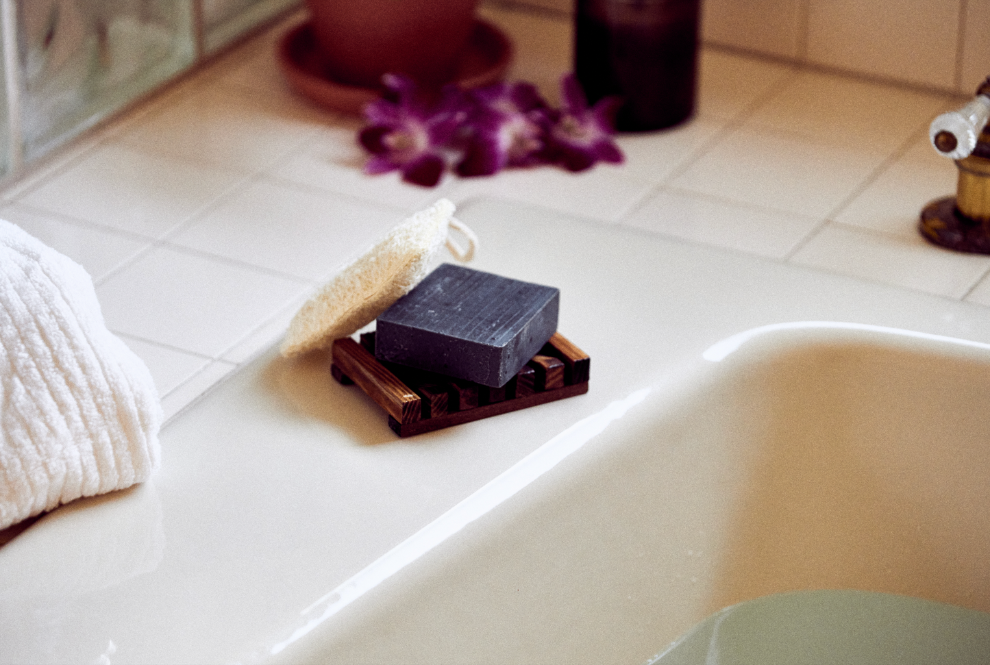 This photo shows the Desesh premium quality US-made small batch body hand and face soap bar with plastic free biodegradable packaging. In the image is a charcoal bar next to a loofah exfoliating pad