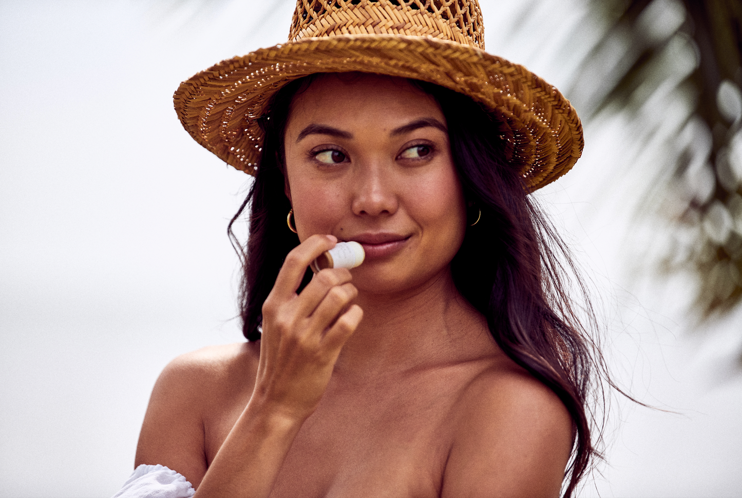 This image shows the Desesh natural plastic free lip balm in a paper based cardboard push up tube for a more eco friendly sustainable zero waste lip balm. In the photo a woman is applying the moisturizing lip balm while smiling