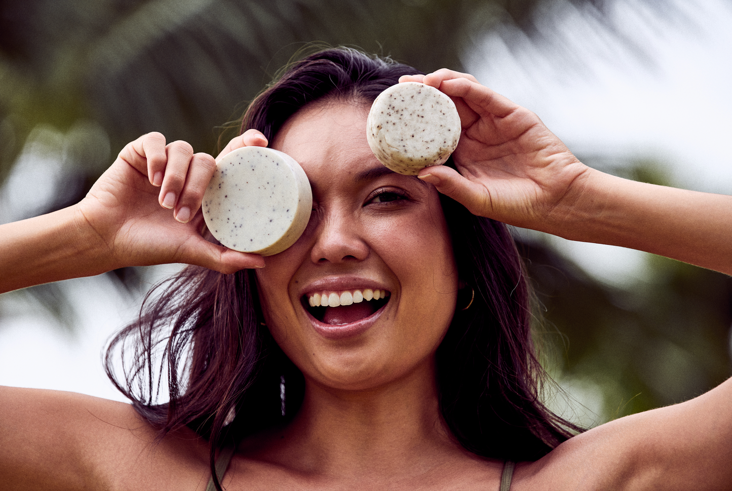 This image shows salon quality Shea Butter solid shampoo bars with plastic free biodegradable packaging for a more sustainable eco friendly zero waste hair care routine. Shown here is a woman holding two of the solid shampoo and conditioner bars next to her face before she washes her hair