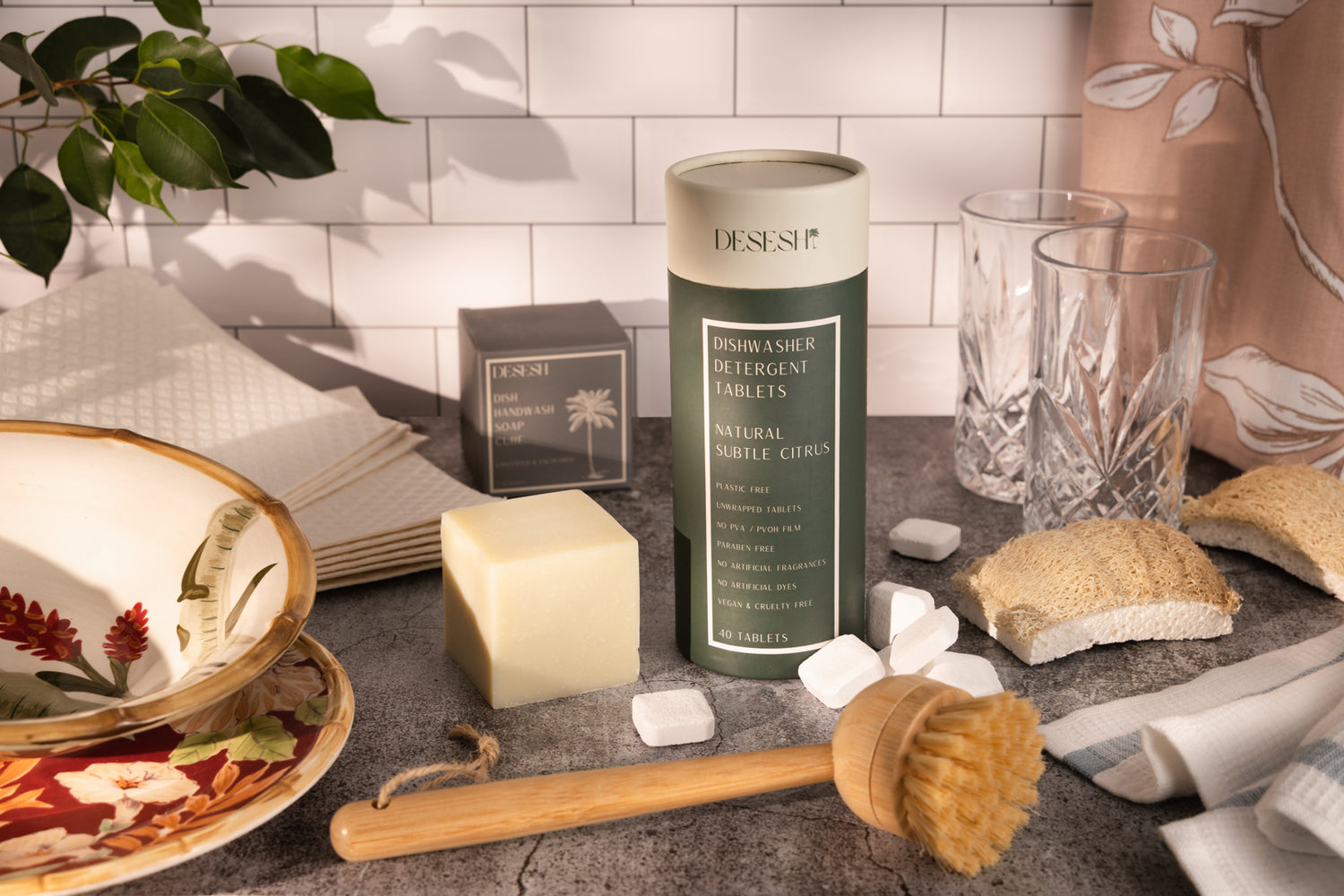 This image shows the Desesh range of plastic free dishwashing products including PVA-free unwrapped dishwasher tablets, dish soap bar, bamboo brush, plant cellulose sponge, and Swedish dish cloths. These are a part of Desesh's range of zero waste, plastic free, eco friendly, more sustainable personal care and everyday essential products.