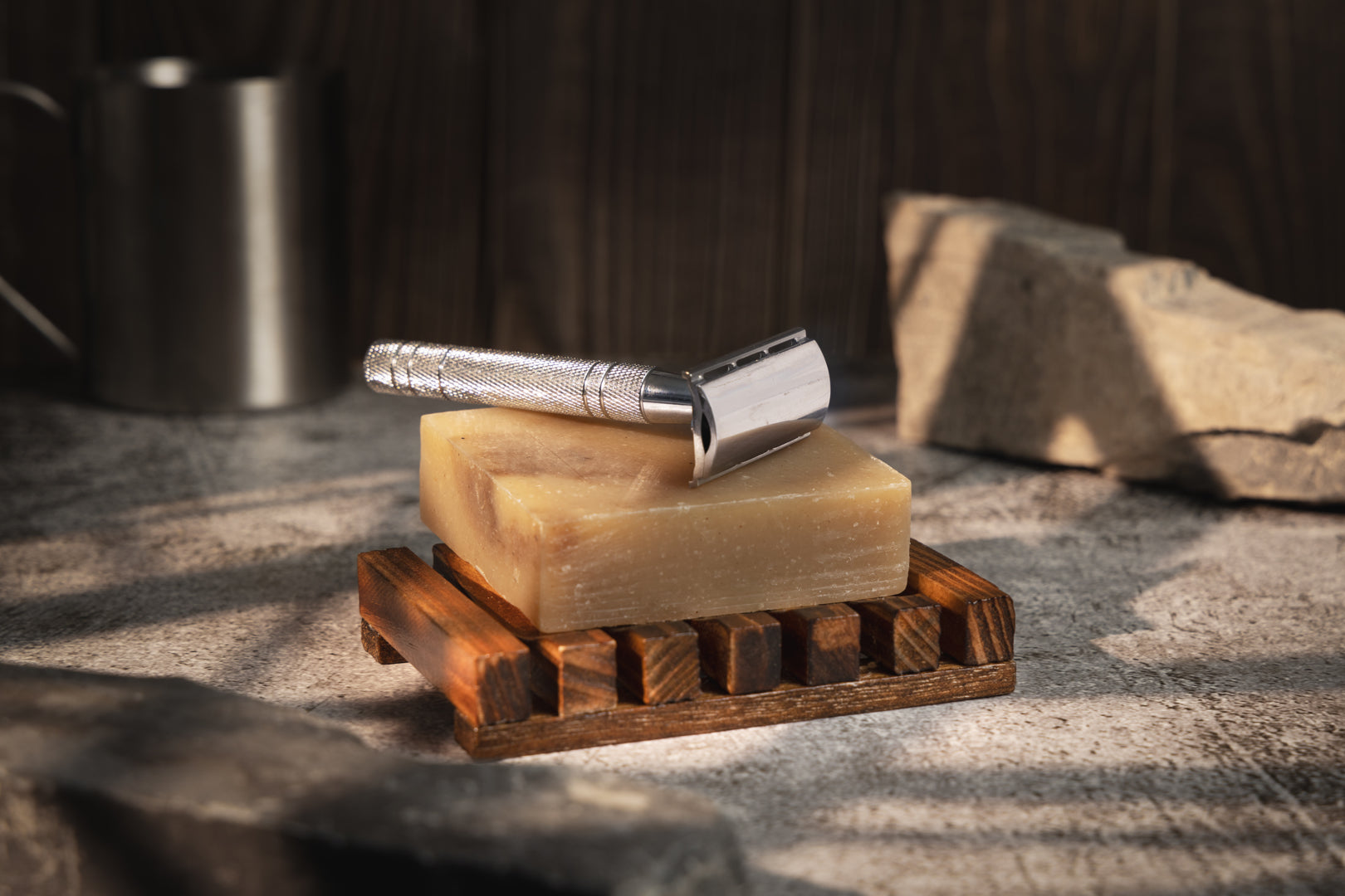 This image shows a dark stained wood soap dish to help keep soap dry. It is rectangular in shape. It is designed for a more eco friendly zero waste sustainable lifestyle and routine. On top of the soap dish is a solid soap bar and a metal reusable safety razor