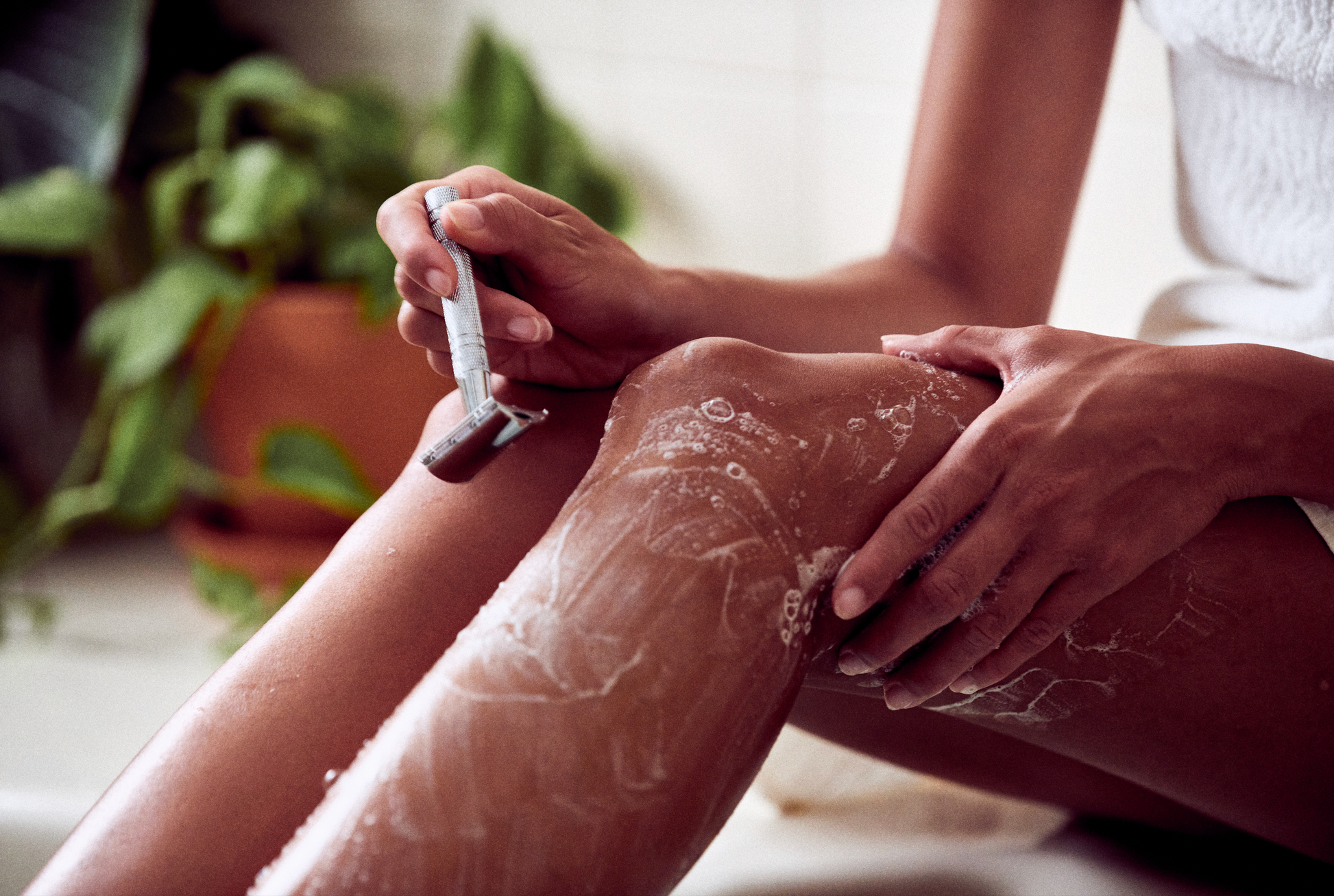 This image shows the Desesh premium quality solid body and face shave soap bar as an alternative to cans of shave foam or cream. This is a more eco friendly sustainable zero waste option and the shave bars come in biodegradable packaging. Shown here is a woman shaving her legs using a solid shave soap bar and a metal reusable safety razor in the bathroom