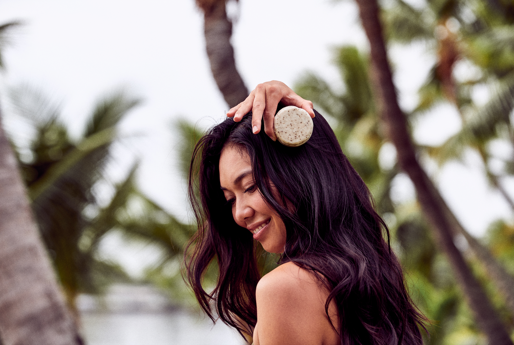 This image shows salon quality Shea Butter solid shampoo bars with plastic free biodegradable packaging for a more sustainable eco friendly zero waste hair care routine. Shown here is a woman holding one of the solid shampoo bars next to her hair before she washes