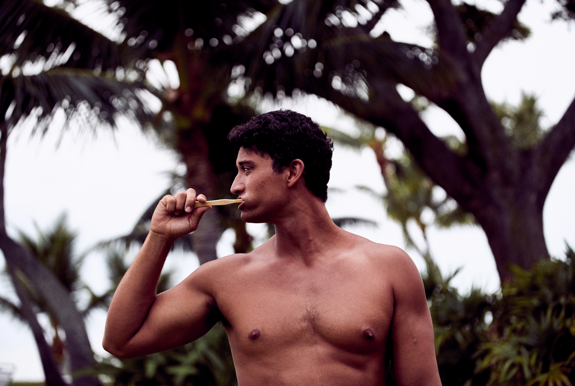 This image shows a shirtless man brushing his teeth with a bamboo toothbrush and US-made fluoride free mint toothpaste tablets
