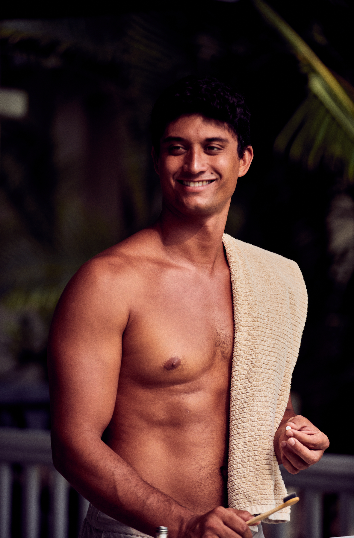 Shirtless man holding US-made fluoride free mint toothpaste tablets and a bamboo toothbrush while smiling